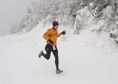 Warmly dressed runner in yellow long-sleeve top and hat running in the snow